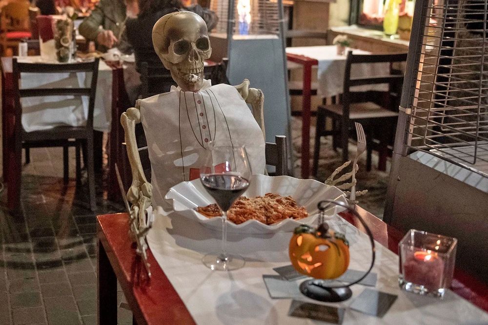 skeleton seated at a restaurant with never ending pasta bowl.