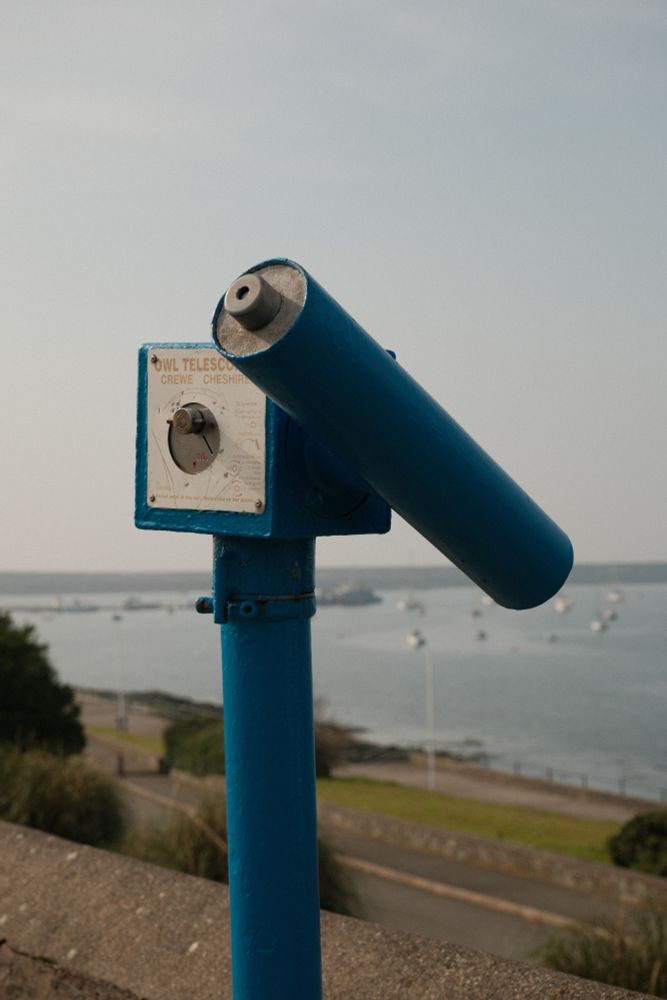 one of those pay to use telescope on the seafront for looking at the distant views, a view of the harbour with boats moored up is visible in the background
