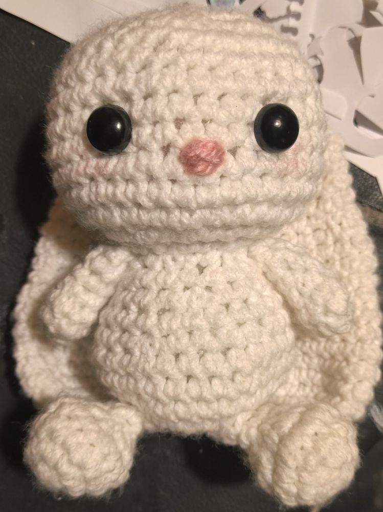 A crocheted white bunny with 2 black eyes and a pink nose