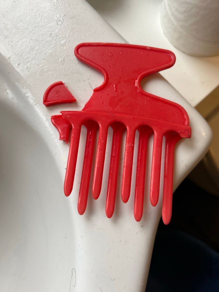 A very battered red Afro comb on a white basin.
