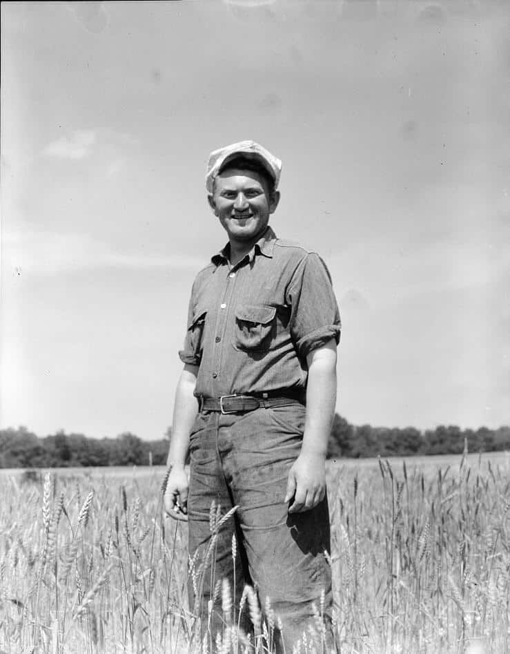 A US farmer stands in a field while wearing a chambray shirt. 