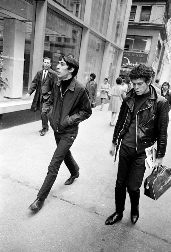 Two men in skinny jeans and boots. They are dressed like rockers. 