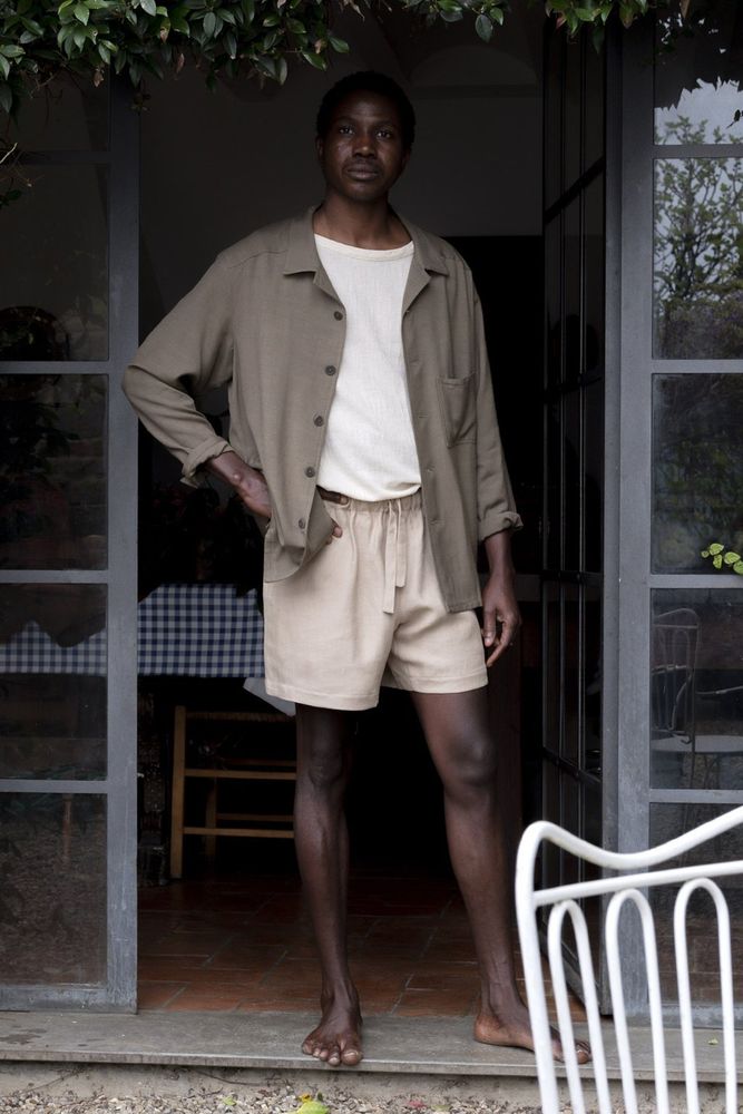 A man is wearing loose fitting tan shorts that end above the knee. He's paired it with a white t-shirt and sage colored overshirt. 
