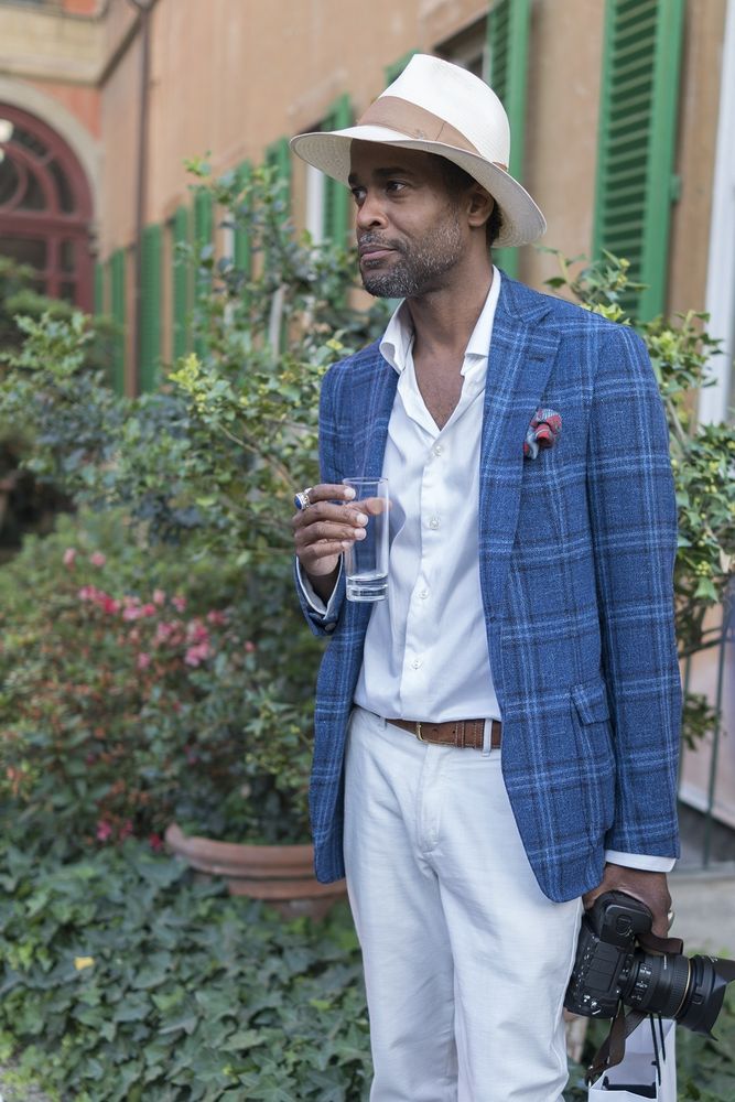 A man wearing a Panama hat with a blue checked sport coat, white dress shirt, and white chinos. 