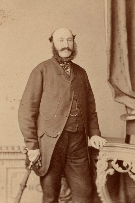 The Duke of Beaufort wearing a long coat, a waistcoat, and a pair of trousers. He also has a tied cravat around his neck.