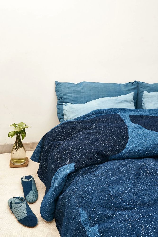 Kantha quilt involving multiple shades and hues of blue. The quilt is sitting on top of a bed.
