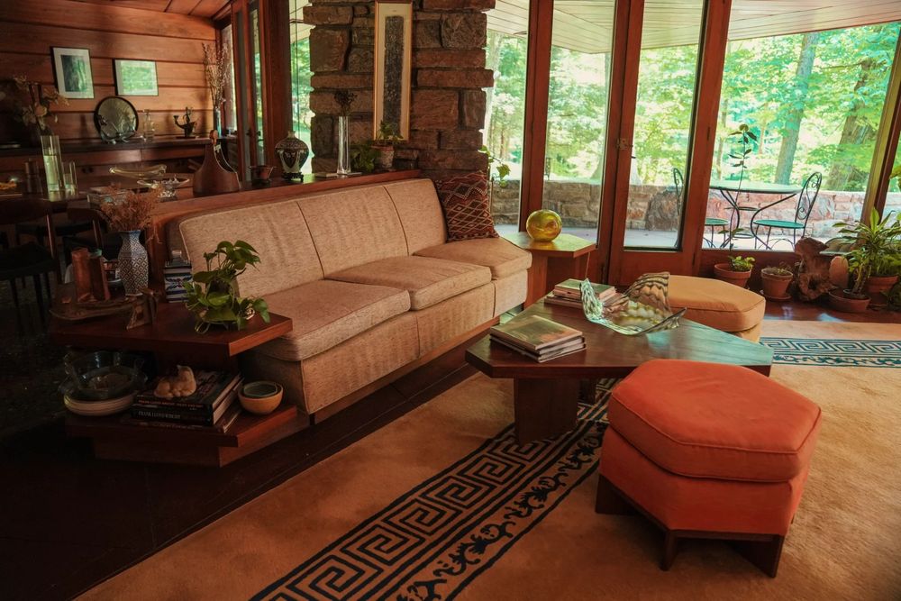 The man's living room. There's a couch, coffee table, and foot stool, as well as some tall windows. Lots of wood. 