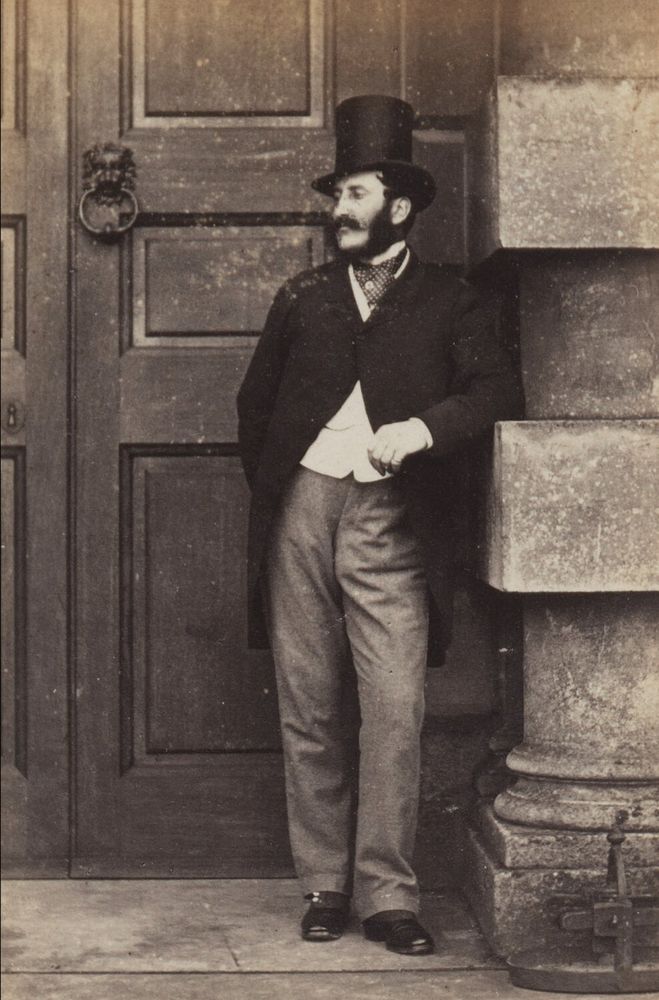 The Duke of Beaufort wearing a long coat, white shirt, a pair of trousers, and a silk top hat. He also has a tied cravat around his neck.