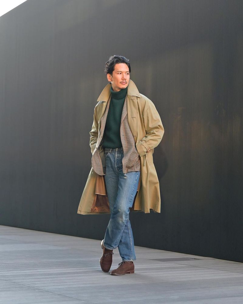 A man wearing vintage chain stitched jeans with a tan raincoat. 