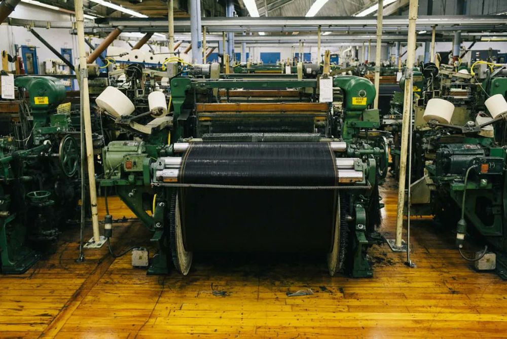 A photo of some narrow width denim being woven on a vintage Drapers' shuttle loom at Cone Mill's White Oak plant in North Carolina. 