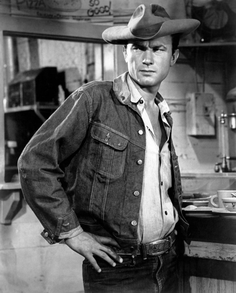 A man in a trucker jacket and some jeans. 