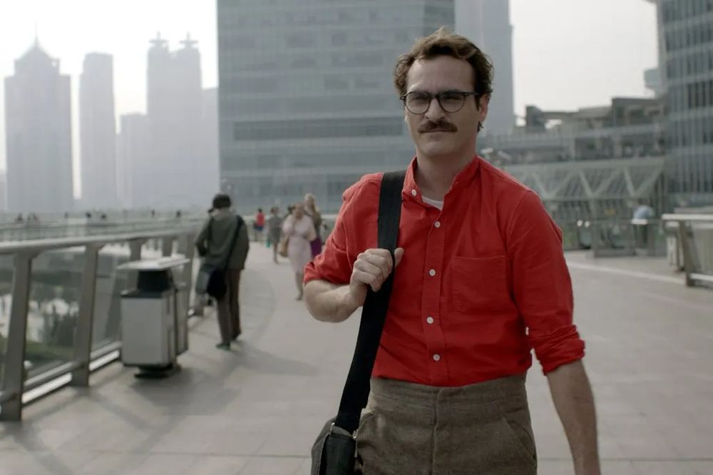 Screenshot from the 2013 film Her. Shows the character wearing brown high-rise trousers with a red button-up shirt. The silhouette is very "of the moment" in 2025.
