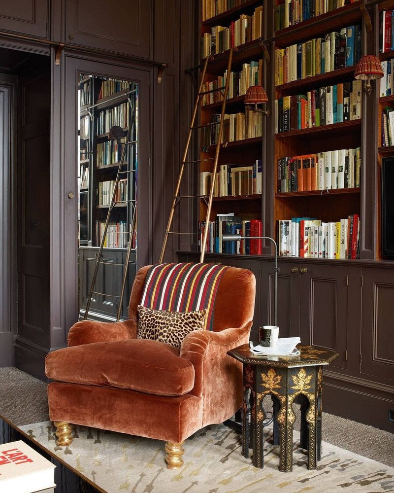A velvet armchair, side table, and brown floor-to-ceiling bookshelves. There's a ladder so you can reach the top shelf. 
