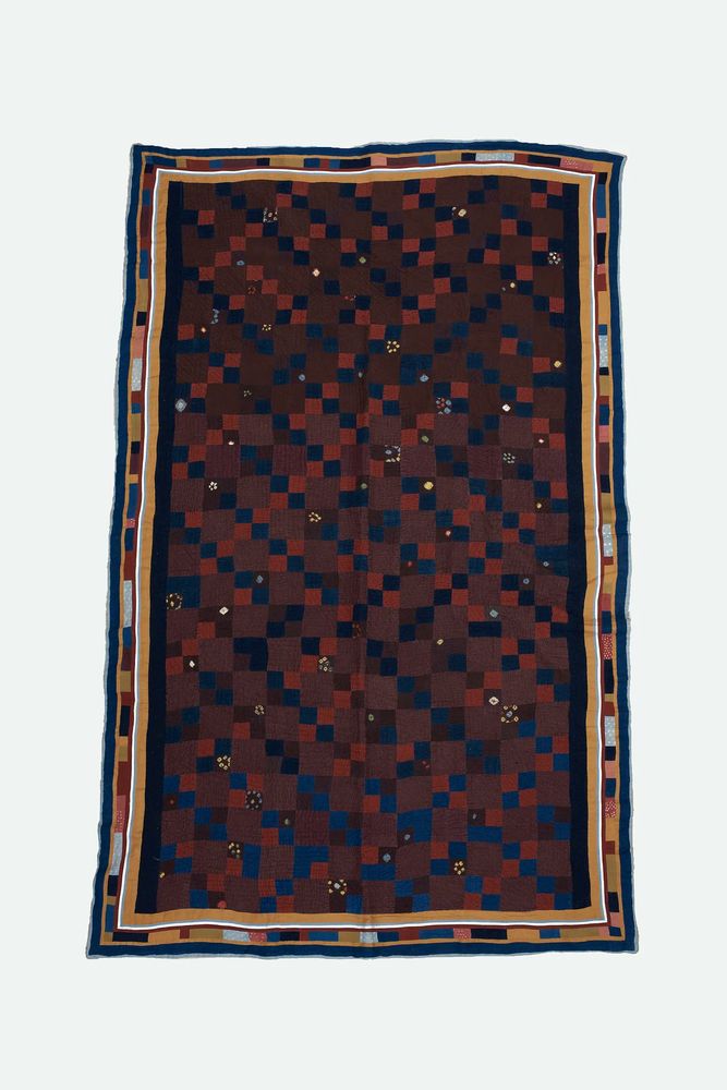 Kantha quilt involving various shades and hues of brown, blue, and red. The motif is made up of various squares. 