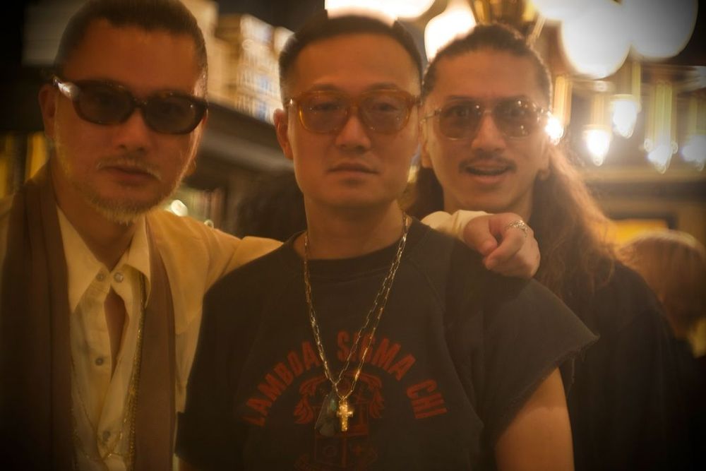 Three men dressed in an alternative style wearing 1970s styled sunglasses