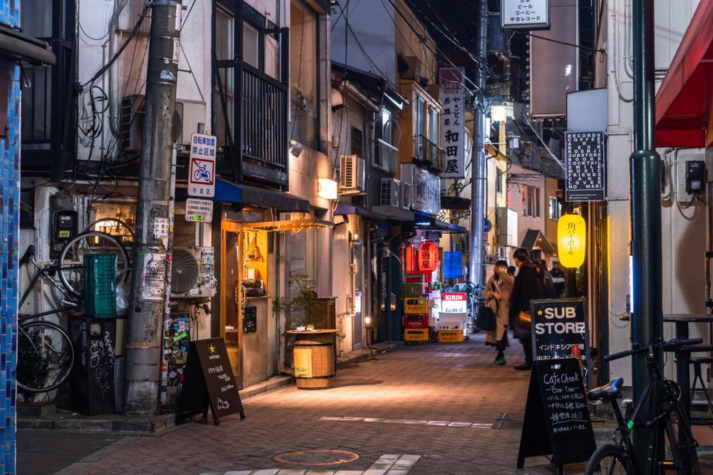 A narrow walkway in Tokyo. The sides of the street are lined with shops and what look to be residences. 