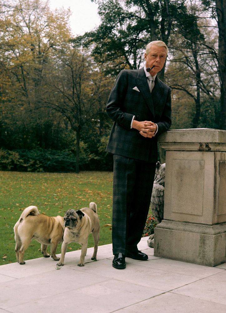 The Duke with two of his dogs. He's wearing a dark checked double-breasted suit with a white shirt and a tie worn with a big knot. 