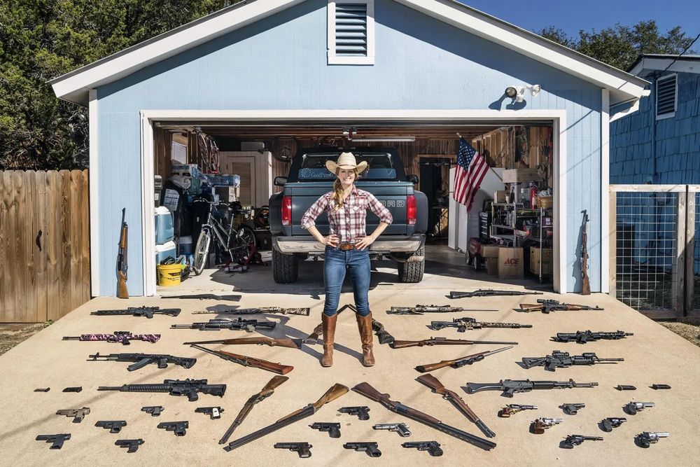 A woman outside her garage. The front of her home is full of guns, some laid out in a star formation. 