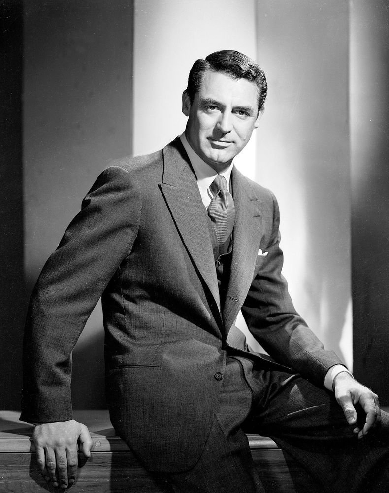 A black-and-white photo of Cary Grant wearing a dark single-breasted peak lapel suit with a white dress shirt and necktie. 