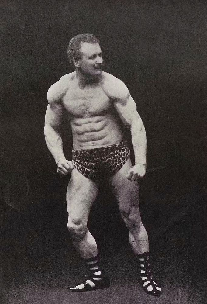 A photo of Eugen Sandow flexing. He's wearing leopard print shorts and gladiator sandals. He's very muscular. 
