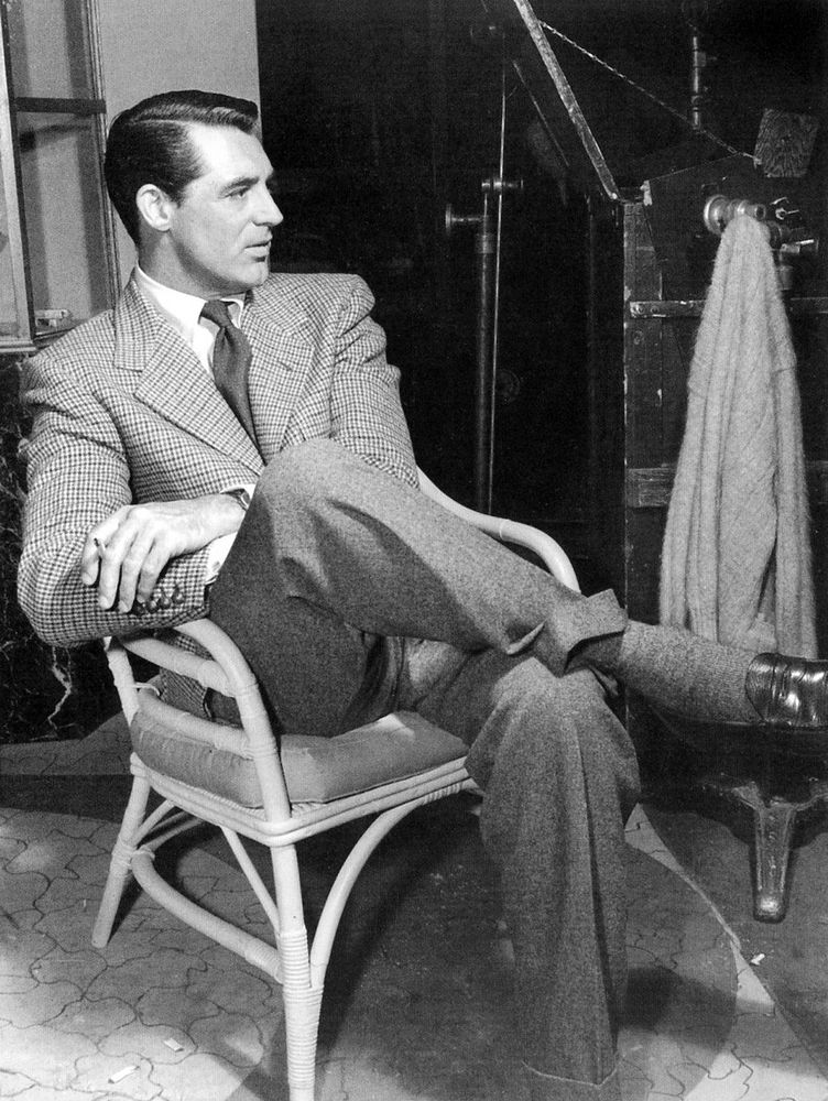 Cary Grant wearing a checked single-breasted sport coat with grey flannel trousers, white button-down shirt, and penny loafers. His tie is worn with a four-in-hand knot. 