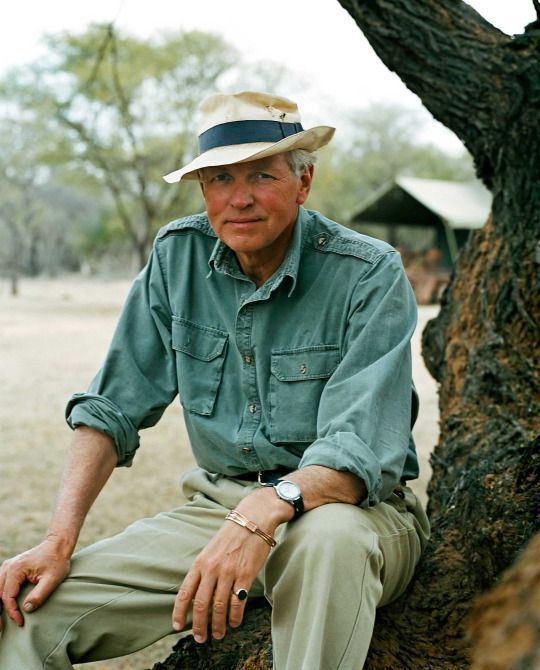 A man in a green field shirt, tan chinos, and a smashed up straw hat. 