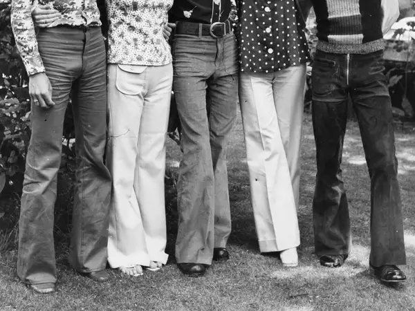 1970s hippies wearing flared pants. There appears to be men and women in the photo, although the image only shows the people from the waist down. 