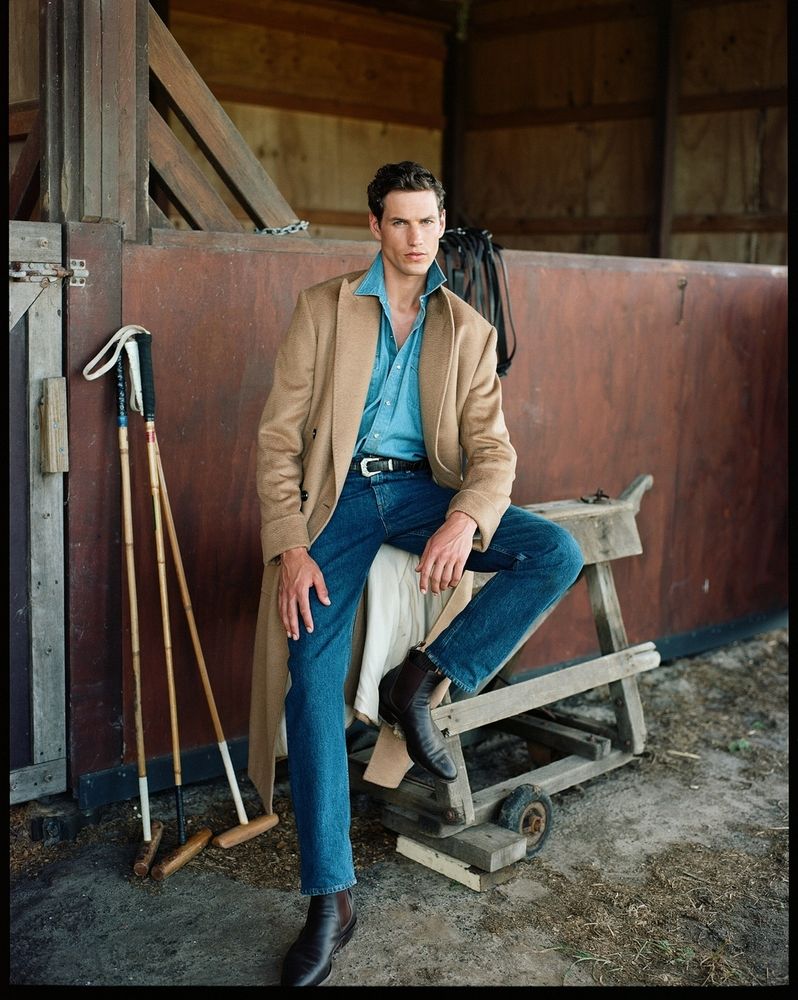 A man wearing pre-washed blue jeans with a tan polo coat. 