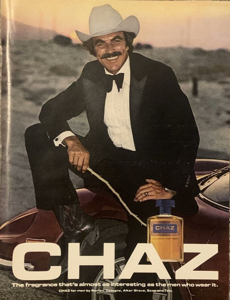 Burt Reynolds in a 1980s ad for a fragrance called Chaz. The byline reads: the fragrance that's almost as interesting as the man who wears it. Reynolds is in a tuxedo, black cowboy boots, white formal shirt, black bow tie, and a cowboy hat. He's in the desert sitting on top of a car. 
