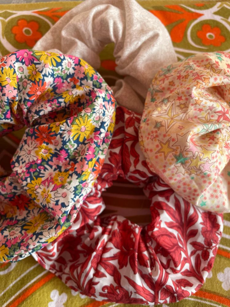 Four scrunchies made from floral tana lawn lying on a green and orange fabric. 
