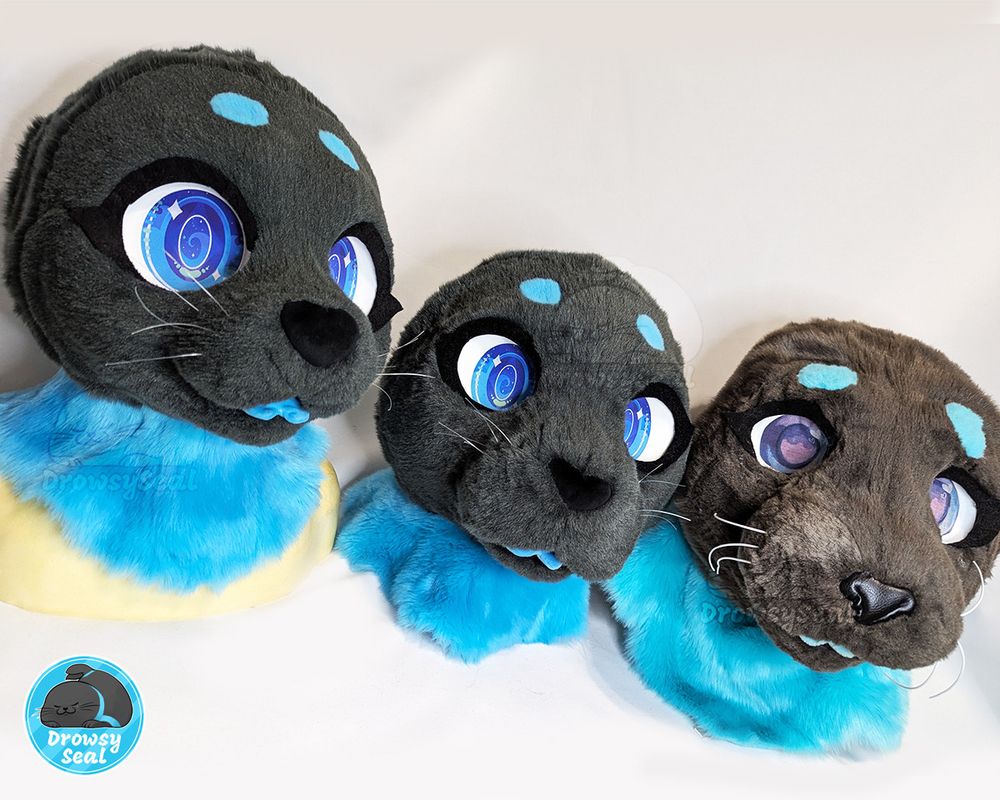 Three fursuit heads of the same ribbon seal character. From left to right: made in 2025, 2023, and 2019.