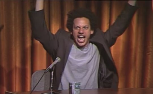 A picture of Eric Andre with his arms up, celebrating. 
