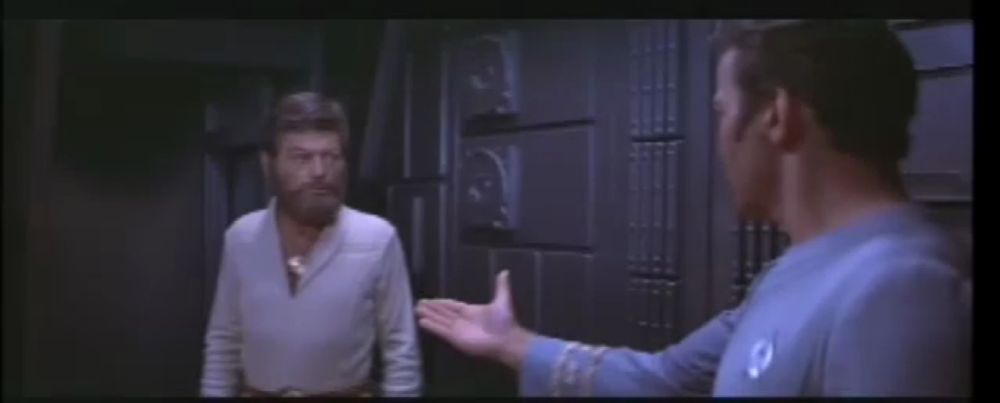 a man in a blue shirt with a star trek logo on his chest talks to another man