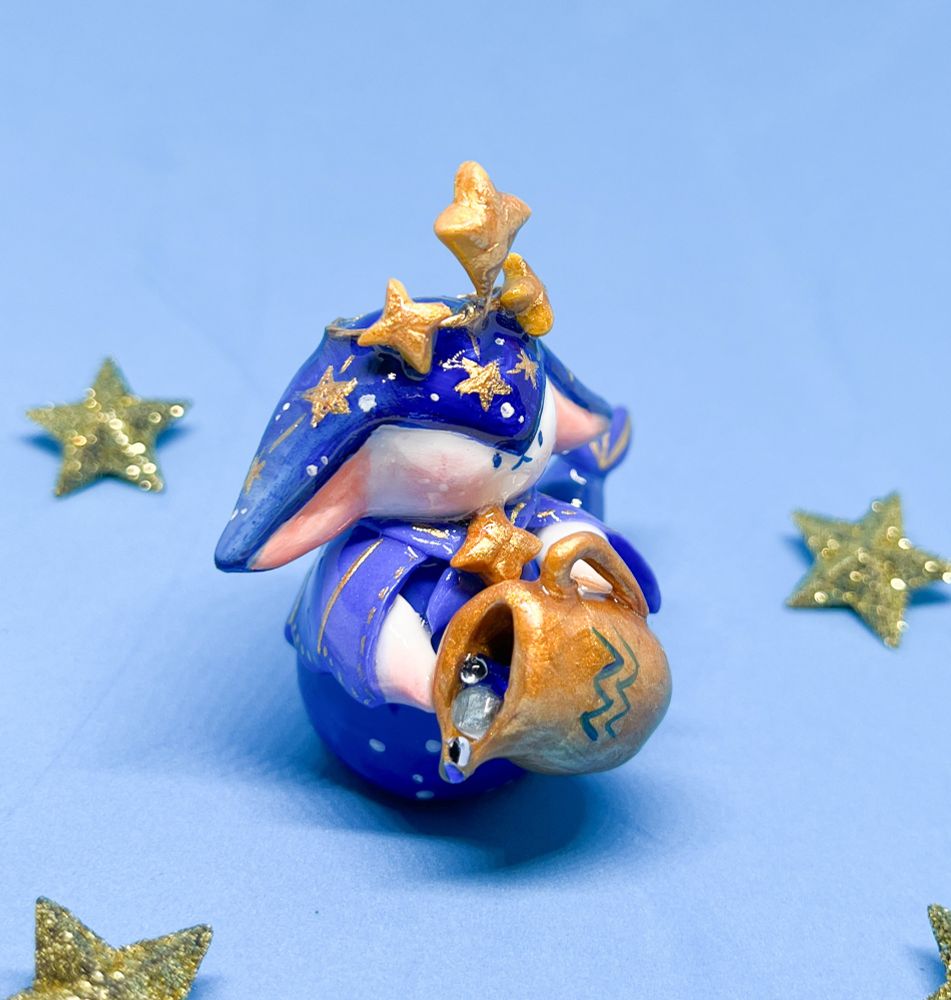A cute clay fantasy character colored in dark blue decorated with golden stars, holding an golden aquarius vase in front of a light blue backdrop 