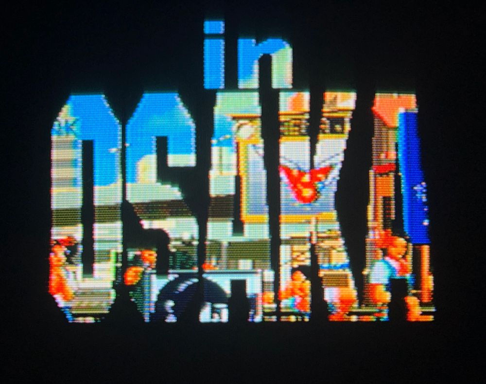 title card for the next fight arrives to frame the next location, the KOF logo is visible on a distant advertisement screen // The King of Fighters 96 for Neo Geo AES, photography on CRT TV 