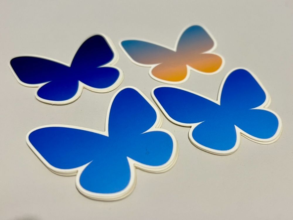 Four Bluesky butterfly logos arranged in a 2x2 grid. Each logo has a different color gradient: two transition from dark blue to light blue, one from midnight blue to dark blue, and one from light blue to orange.