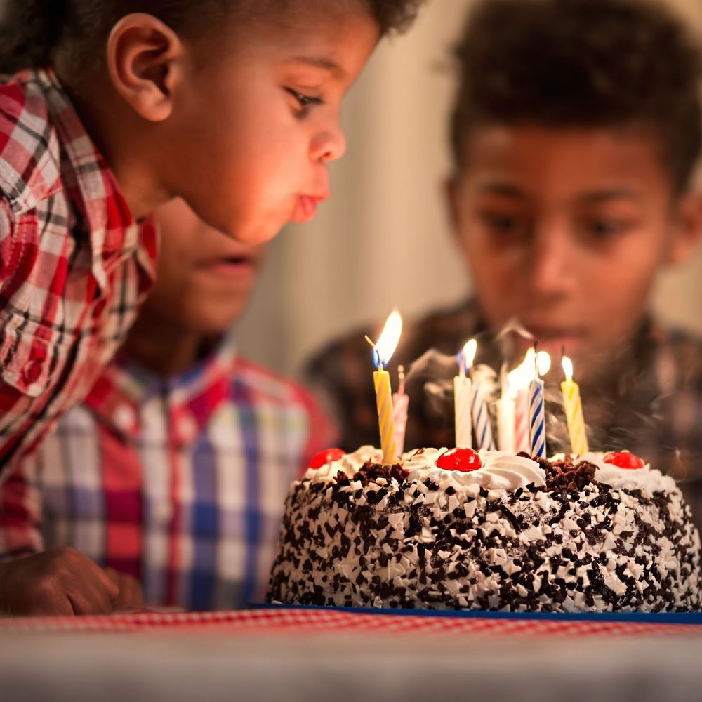 A young boy blows out candles on a cade, with other children in the background