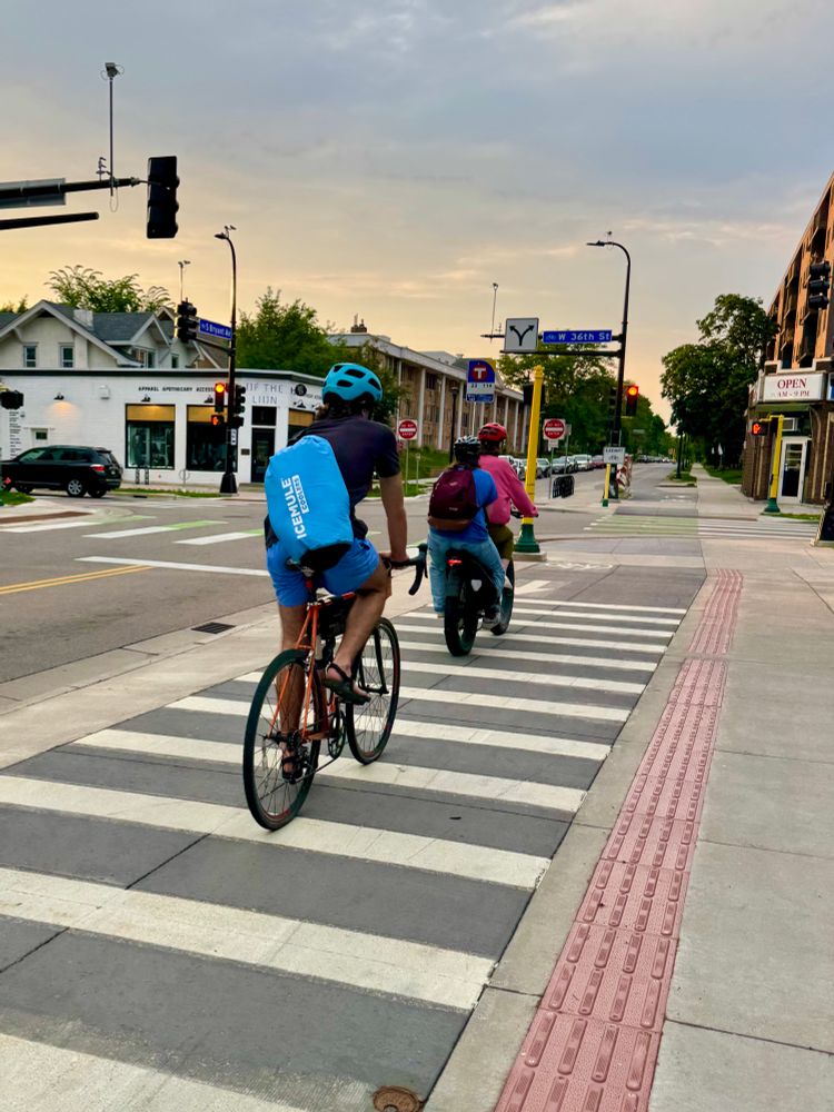 Two bikes on a sidewalk level bikeway at sunset. One of the bikes is an e cargo bike with an adult passenger