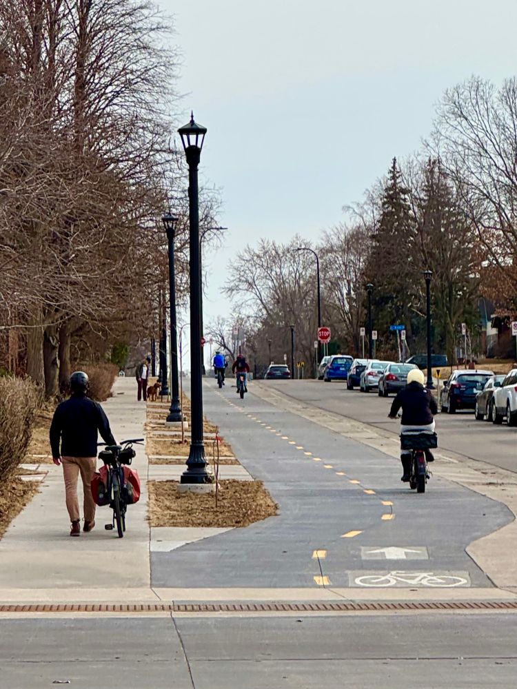Well designed street with a sidewalk level 2 way bikeway, narrow lane for cars, and sidewalks on both sides. Many people are walking & biking. No one is driving.