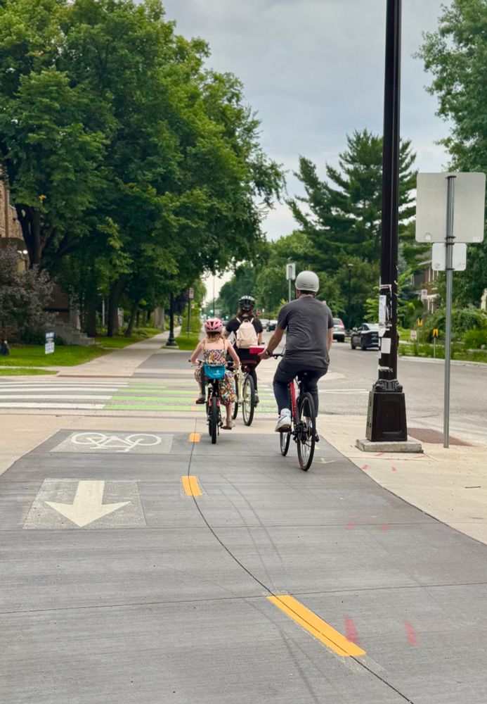 Two parents and a young kid bike together down Bryant Ave S (two way protected bikeway)