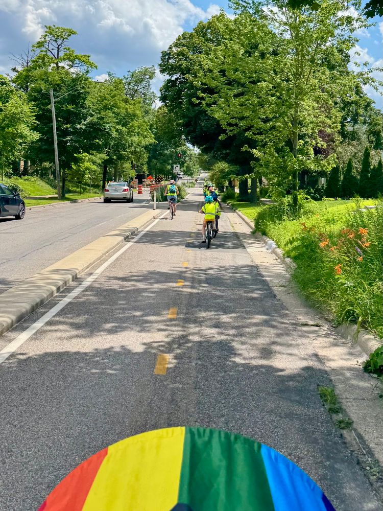 Group of 20 elementary schoolers bike in the Blaisdell 2 way curb protected bikelane. They wear high viz vests.