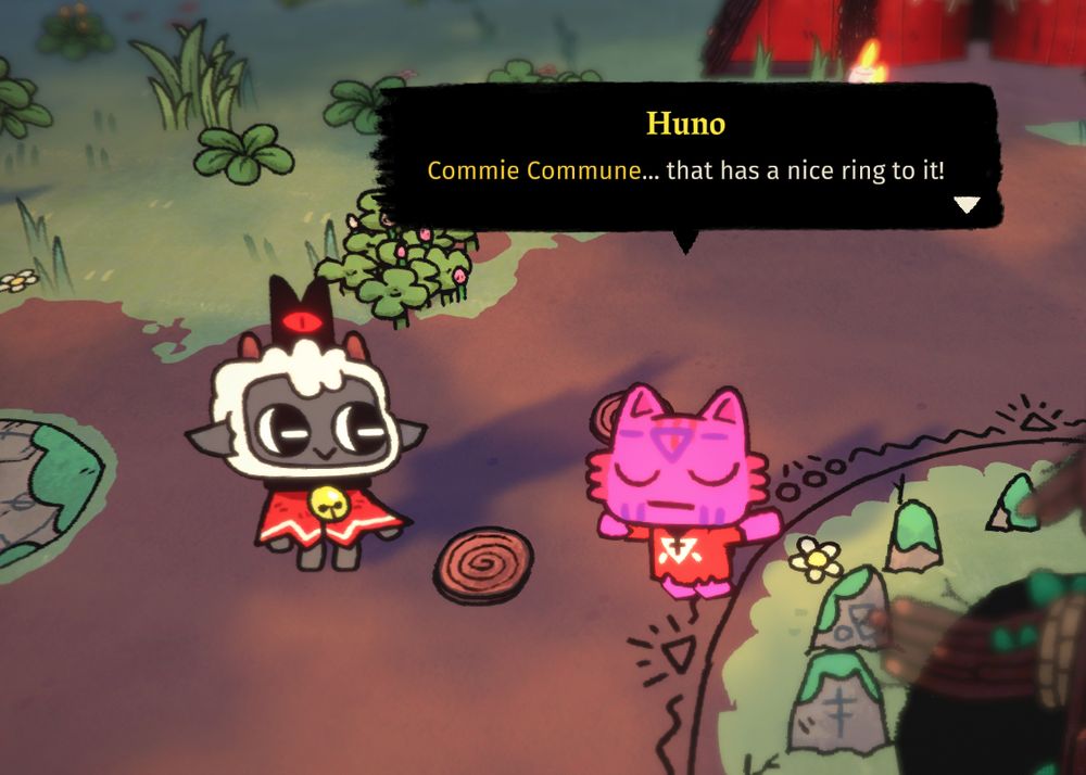 colorful cartoon screenshot of the game Cult of the Lamb, with the lamb (my character) smiling nodding at the pink cat saying "Commie Commune... that has a nice ring to it!"