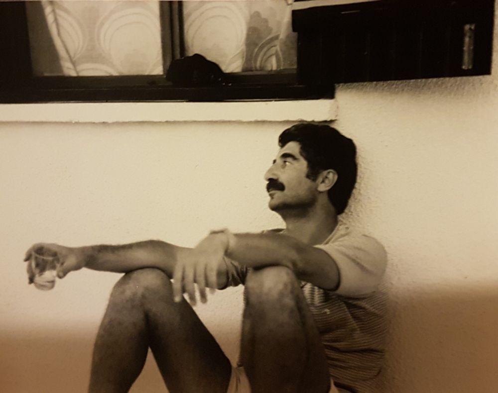 Picture of a man in the 80s sitting in front of a wall.