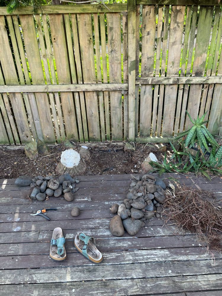 A pile of large stones on an old brown deck which have been pulled from a garden bed