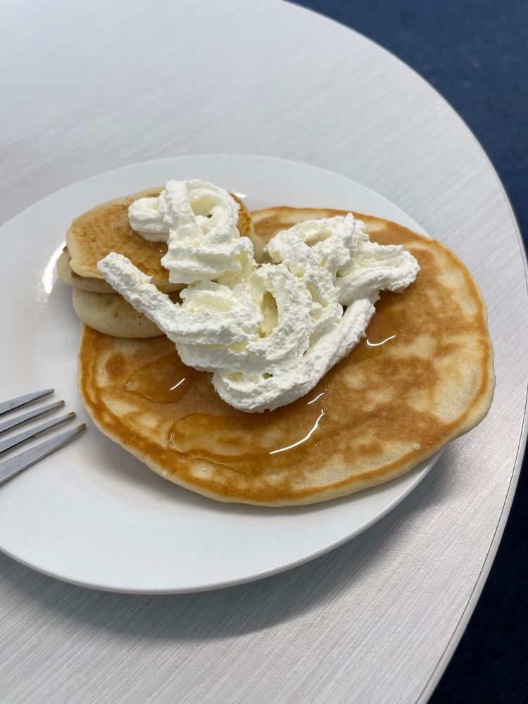 A plate with pancakes covered in syrup and whipped cream 