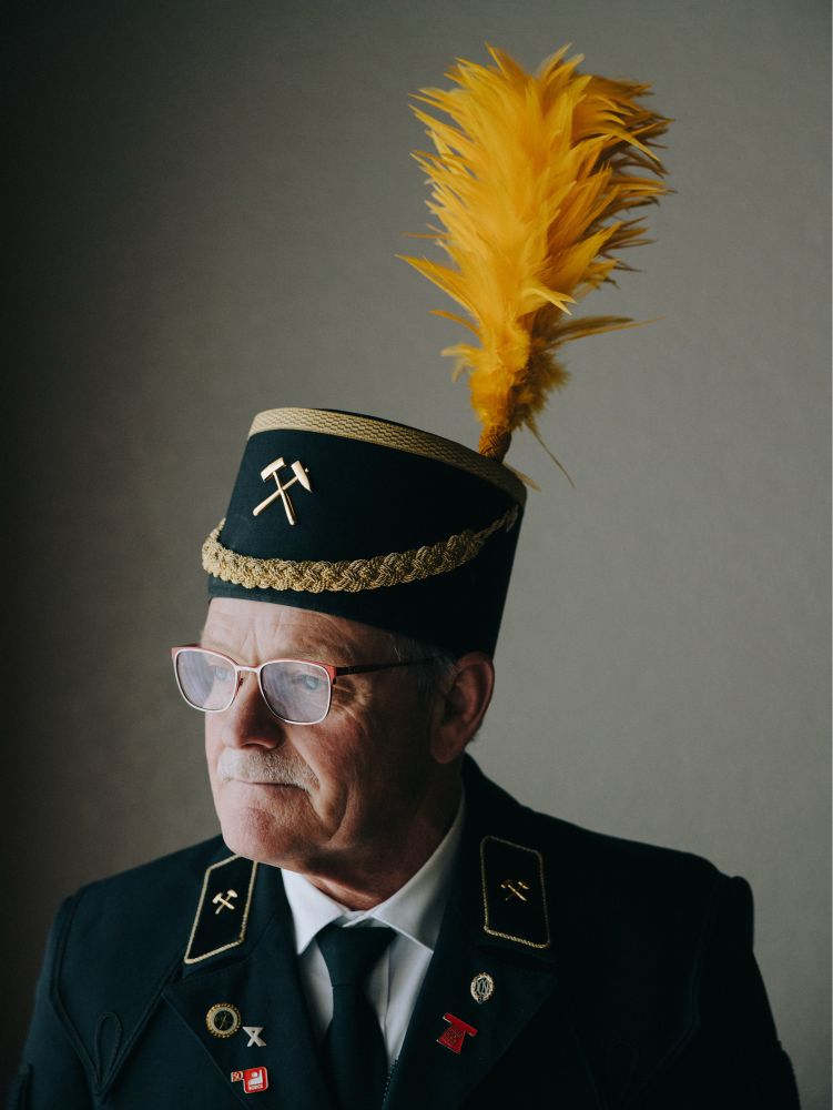 Close-op of a miner posing for a portrait. He’s looking to his left, the direction of the soft light of the window. His silhouette is very characteristic with the bushy shape of the yellow plume on top of his shaft hat.