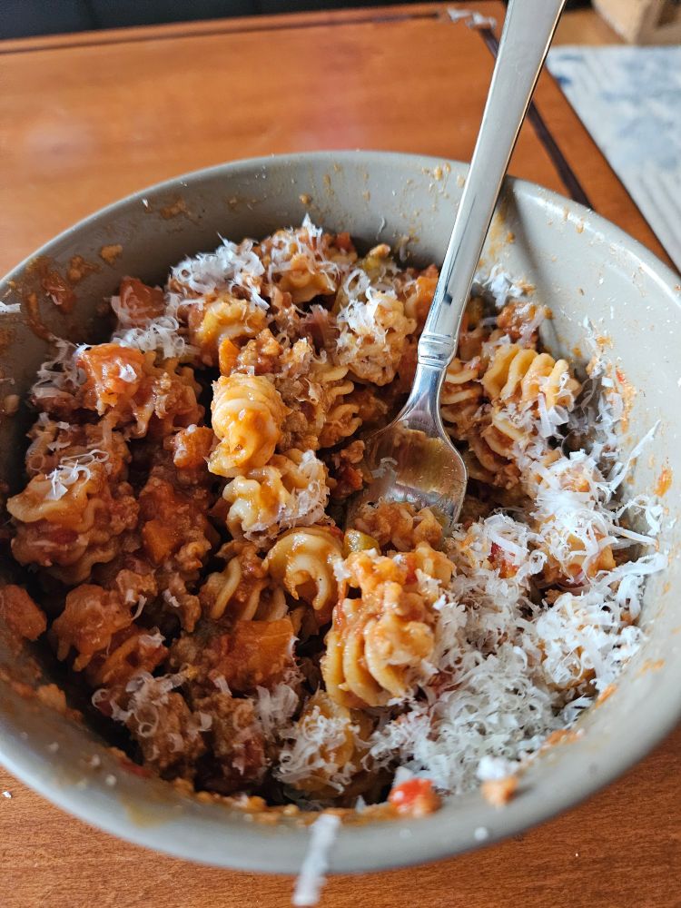 Picture of a bowl of radiatore pasta tossed in  a sausage ragu topped with Parmigiano Reggiano cheese and fresh grated nutmeg. 