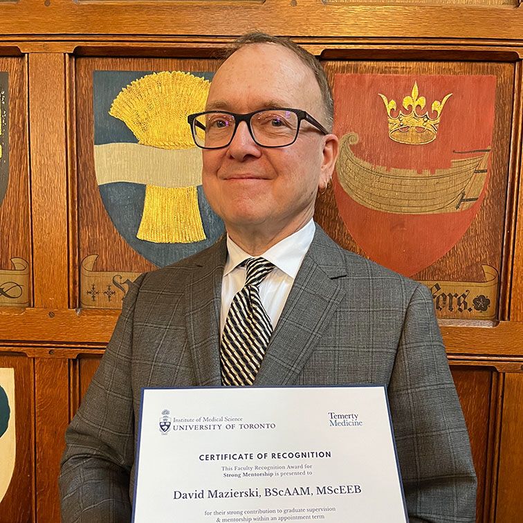A man in a suit holds an award certificate.