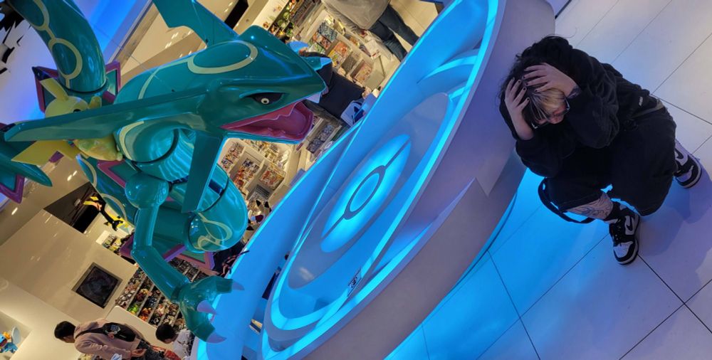 A person covers in the corner as a large figurine of the pokemon rayquaza hovers above them