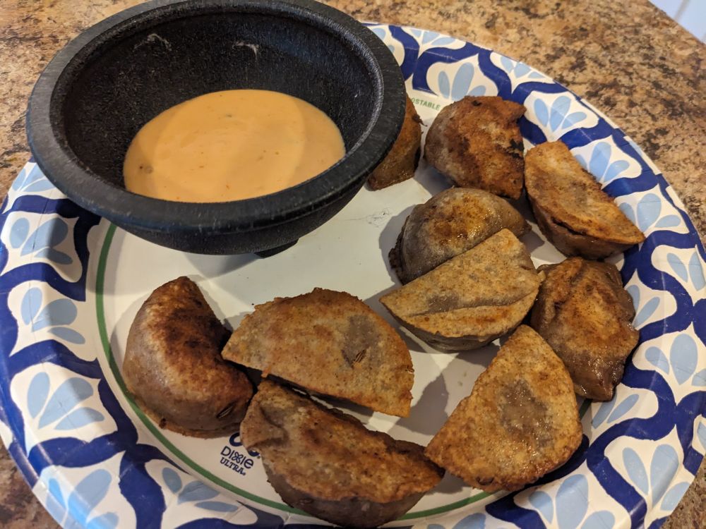 Some of the boiled and fried pierogi on a paper plate with a bowl of Thousand Island dressing.